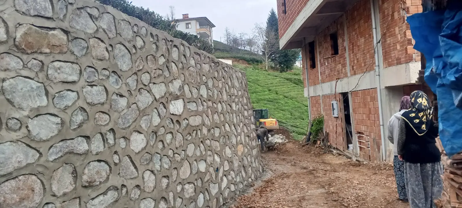 Bina yanında taş duvar ve iş makinesiyle saha çalışması